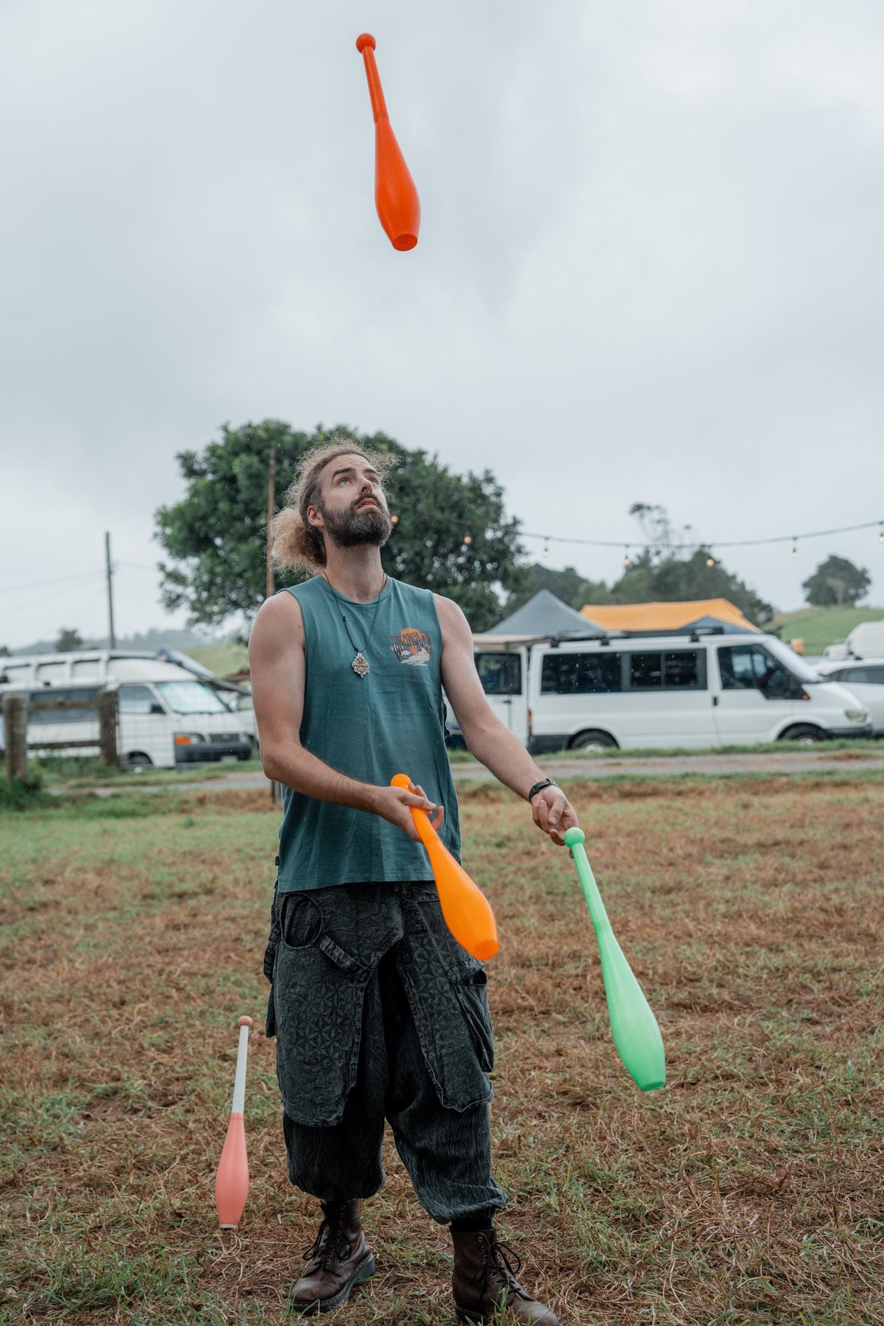Juggler tossing orange and green clubs above his head at a daytime bush festival
