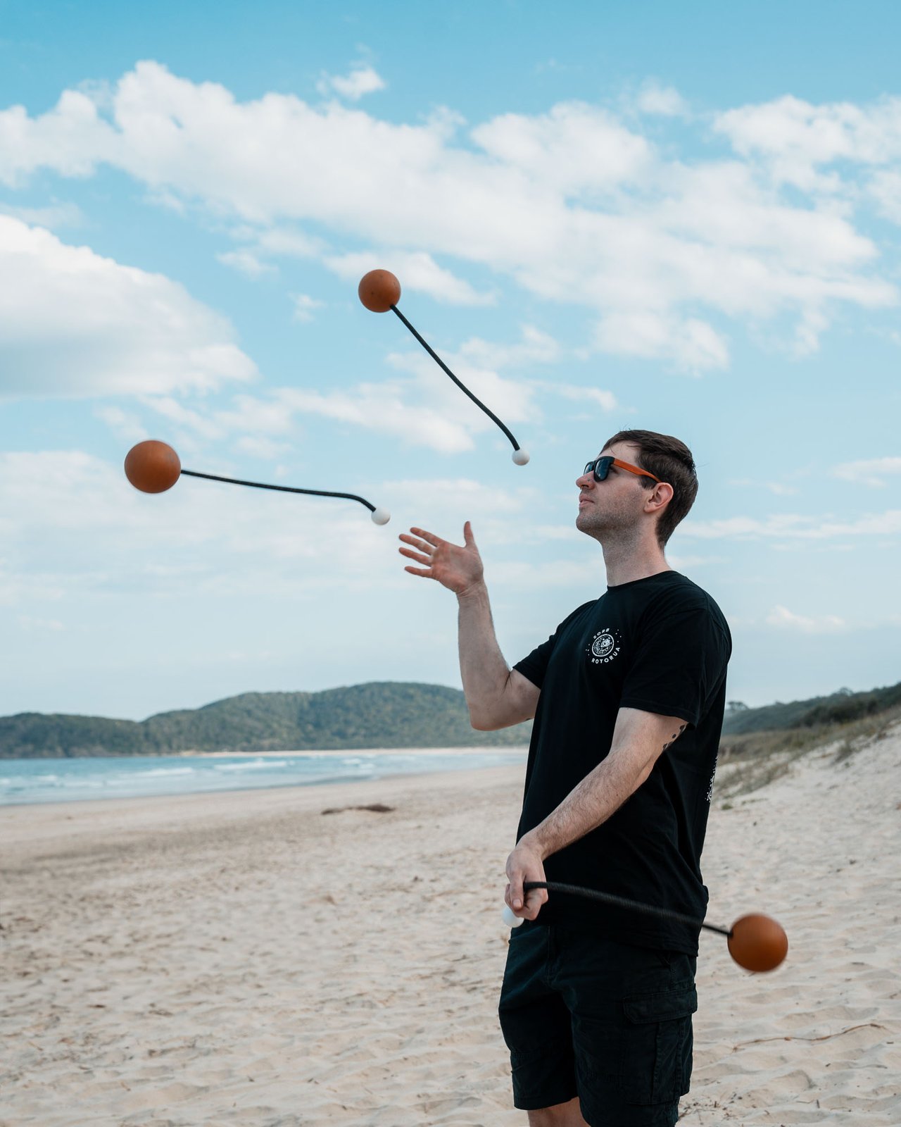 Beach juggler practising sphere poi in mid-air on a sunlit headland beach