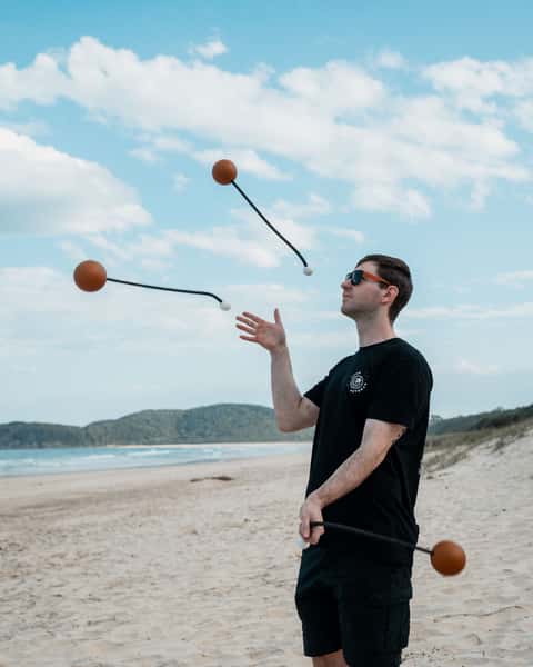 Beach juggler practising sphere poi in mid-air on a sunlit headland beach