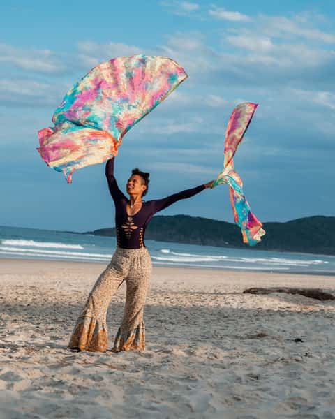 Performer flowing rainbow silk scarves on an open coastal beach in late-afternoon light