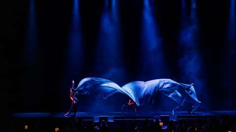 Two aerial silks performers throwing huge silver silks under deep blue beam light at Cirque Bon Bon