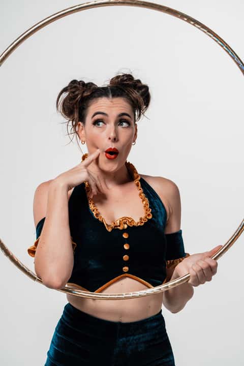 Cirque hoop performer in deep teal velvet costume holding a brass hoop, white studio backdrop