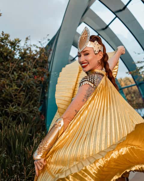 Costumed character performer in pleated gold cape and crown, outdoor pavilion light