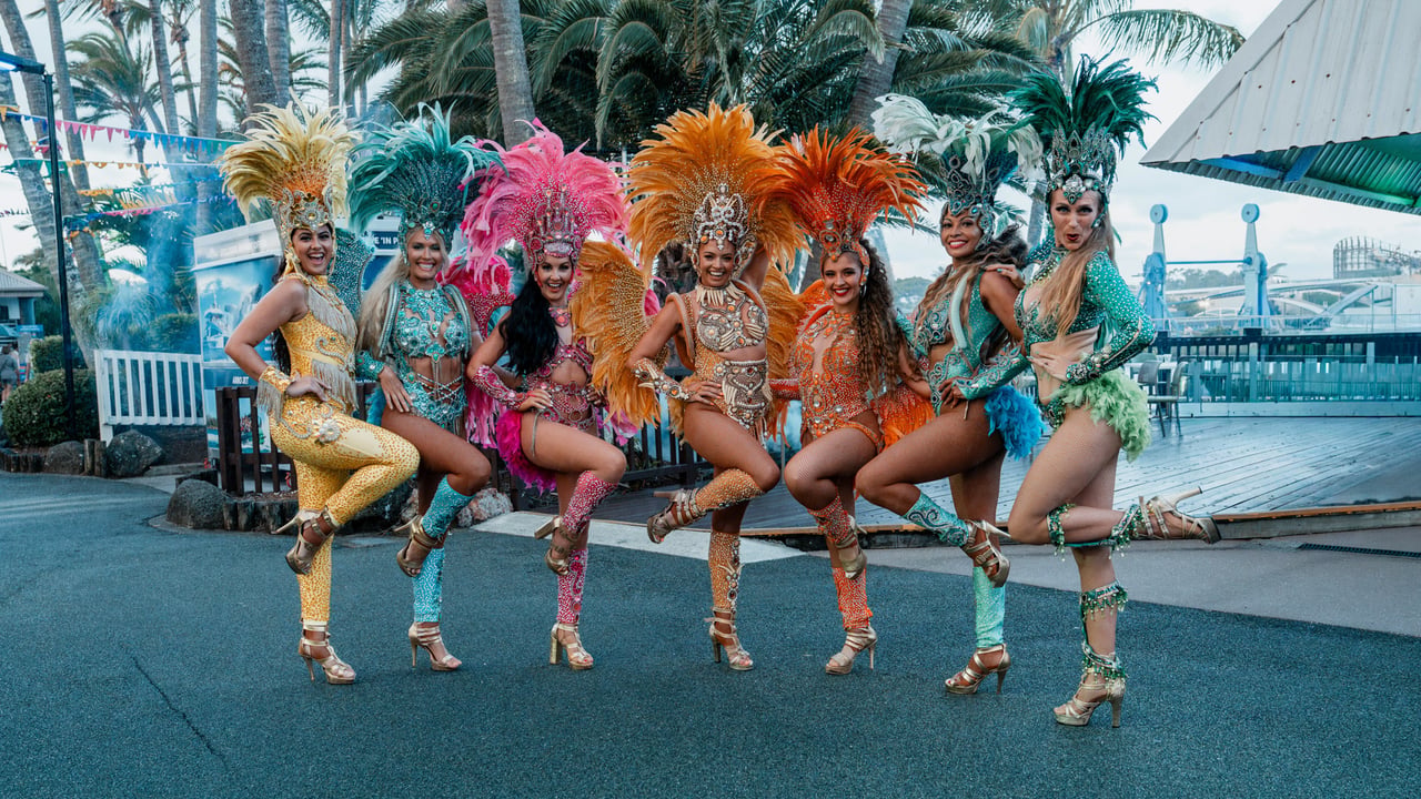 Samba dance troupe in oversized feathered headdresses lined up outside under daylight