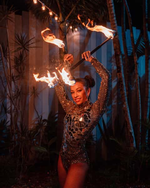 Fire performer spinning flame poi in costume against palm trees in tropical evening light