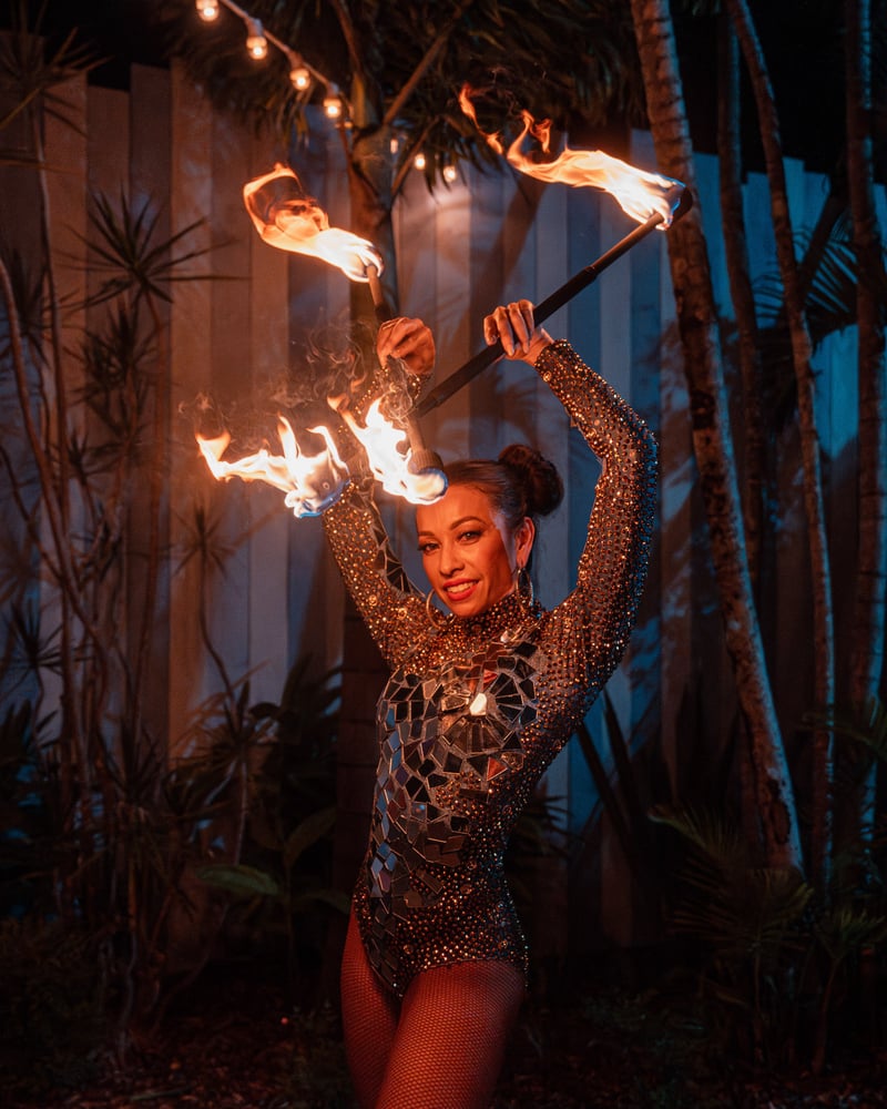 Fire performer spinning flame poi in costume against palm trees in tropical evening light