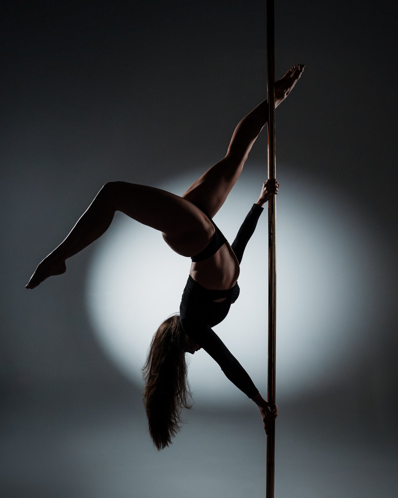 Pole performer alternate frame, controlled studio dark, vertical pole visible