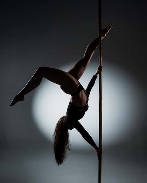 Pole performer alternate frame, controlled studio dark, vertical pole visible