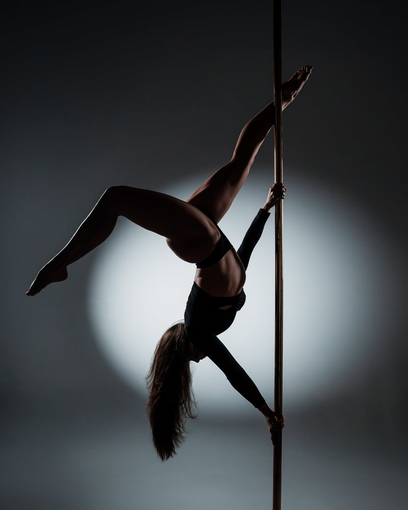 Pole performer alternate frame, controlled studio dark, vertical pole visible