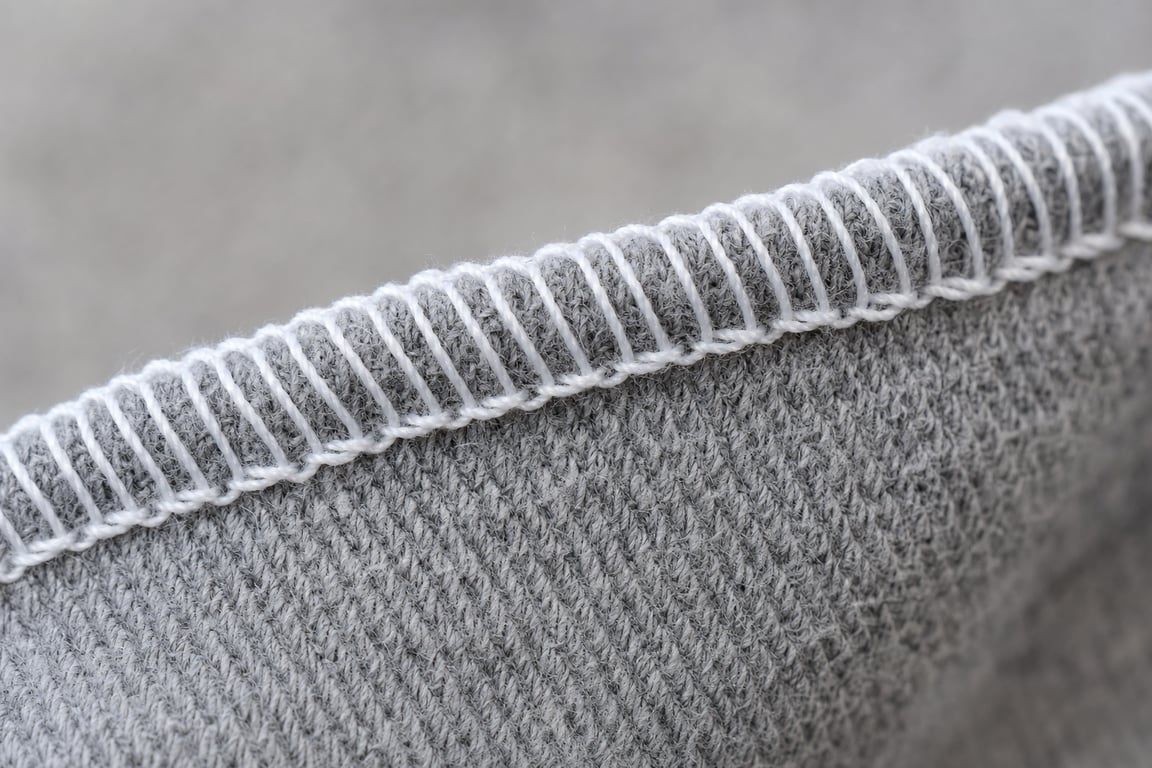 Close-up of a gray jersey fabric edge wrapped in a neat white serged overlock stitch