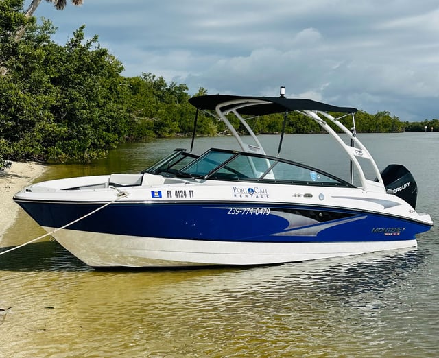 A blue and white Monterey rental deck boat from Port O Call Marina moored along a mangrove-lined sandbar