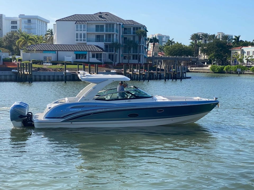 A blue and white Formula sport boat cruising calm bay water past waterfront condos and docks