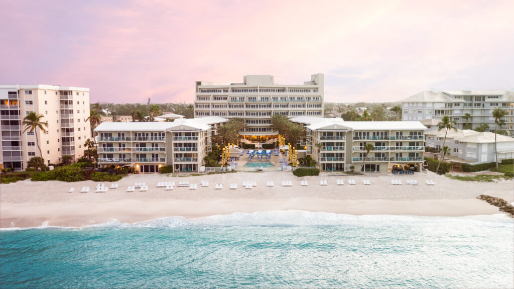 Aerial view of Edgewater Beach Hotel at sunrise with white lounge chairs lining the sand and turquoise Gulf waves
