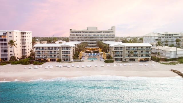 Aerial view of Edgewater Beach Hotel at sunrise with white lounge chairs lining the sand and turquoise Gulf waves
