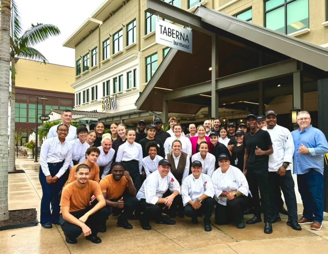 Large staff team in chef coats and white shirts posing outside Taberna Burntwood beneath the restaurant sign
