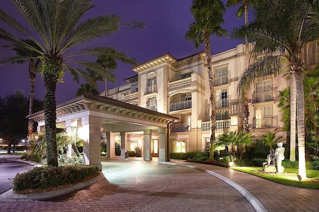 Illuminated porte-cochere entrance and palm-lined driveway at Trianon Bonita Bay at dusk