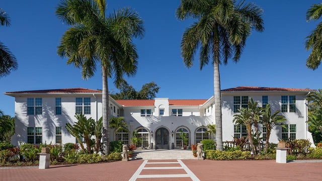 Shangri-La Springs, a white Mediterranean-style building with red tile roof framed by tall royal palms under blue sky