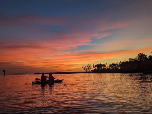 Two kayakers silhouetted on calm water beneath a pink and orange sunset sky on a Naples sunset kayak tour