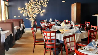 Dining room at Amber Cove with white-clothed tables, navy napkins, red wood chairs and a lit branch sculpture