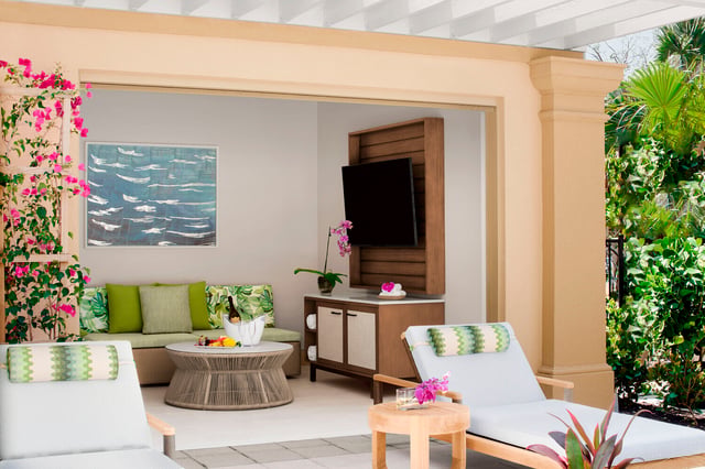 Poolside cabana at The Ritz-Carlton, Naples with green cushioned lounge chairs, a TV, and blooming bougainvillea