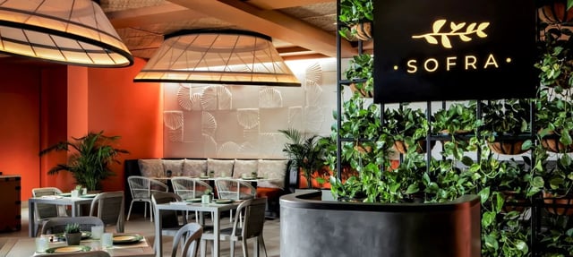 Sofra restaurant interior with a black sign, hanging woven pendant lights, greenery wall and set dining tables