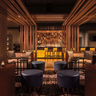 Dimly lit lounge at DUSK with leather ottomans, wood slat partitions and a glowing backlit bar