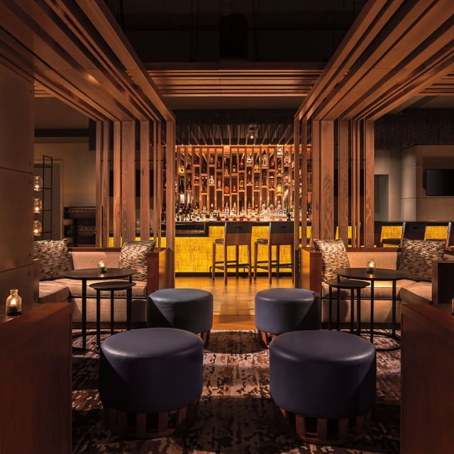 Dimly lit lounge at DUSK with leather ottomans, wood slat partitions and a glowing backlit bar