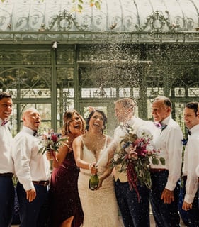 Bride and wedding party celebrating with a champagne spray outside the glass conservatory at Wonder Gardens