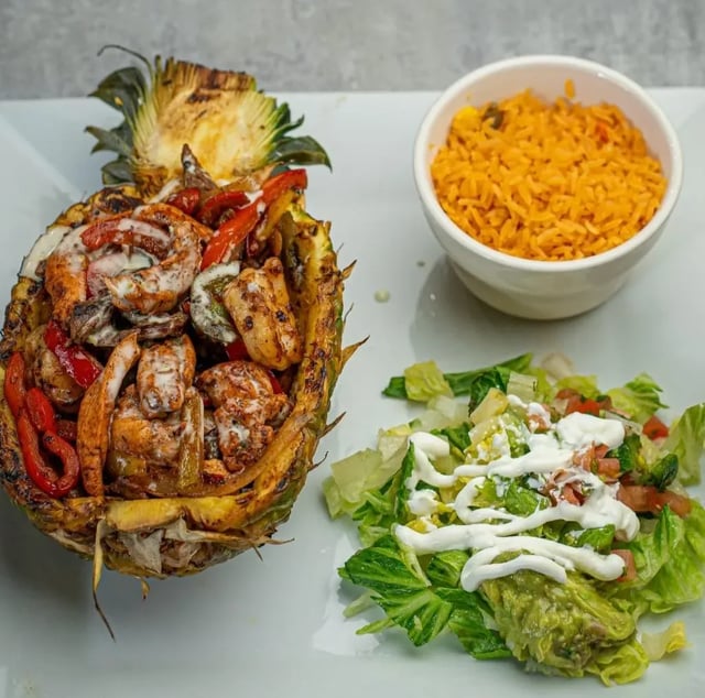 Grilled shrimp and peppers served in a hollowed pineapple half with Mexican rice and a garnished salad at 1942 Mexican Grill