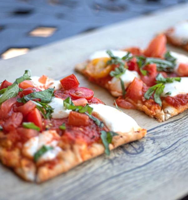 Squares of margherita flatbread topped with fresh mozzarella, chopped tomatoes and basil on a wooden board