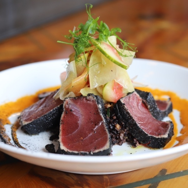 Seared rare tuna crusted in black sesame, topped with shaved vegetables and pea shoots on a white bowl at The Oyster Society