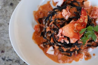 Squid ink pasta twirled in a tomato cream sauce with lobster claw meat and parsley on a white plate