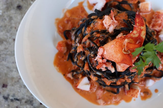 Squid ink pasta twirled in a tomato cream sauce with lobster claw meat and parsley on a white plate