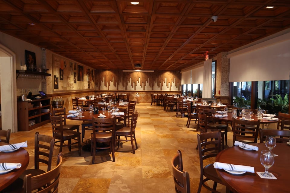 Warmly lit dining room at DaVinci's with a coffered wood ceiling, stone tile floors and set tables