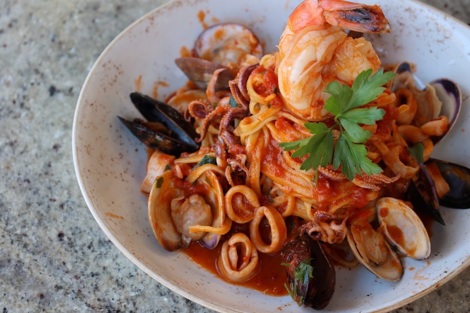 Seafood pasta with shrimp, mussels, clams and calamari in red sauce, topped with parsley, in a white bowl