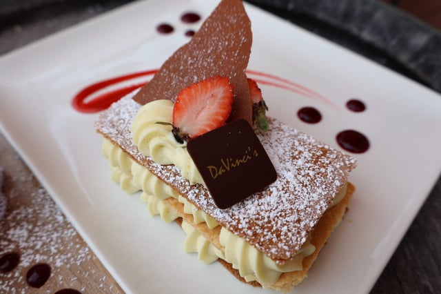 Layered napoleon pastry with cream, strawberry and a chocolate square stamped DaVinci's on a white plate