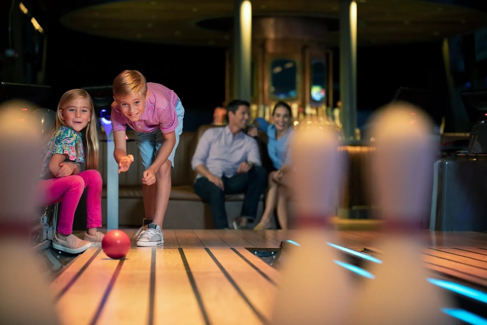 A boy rolls a red ball down a glowing lane while a girl and parents watch at 10K Alley
