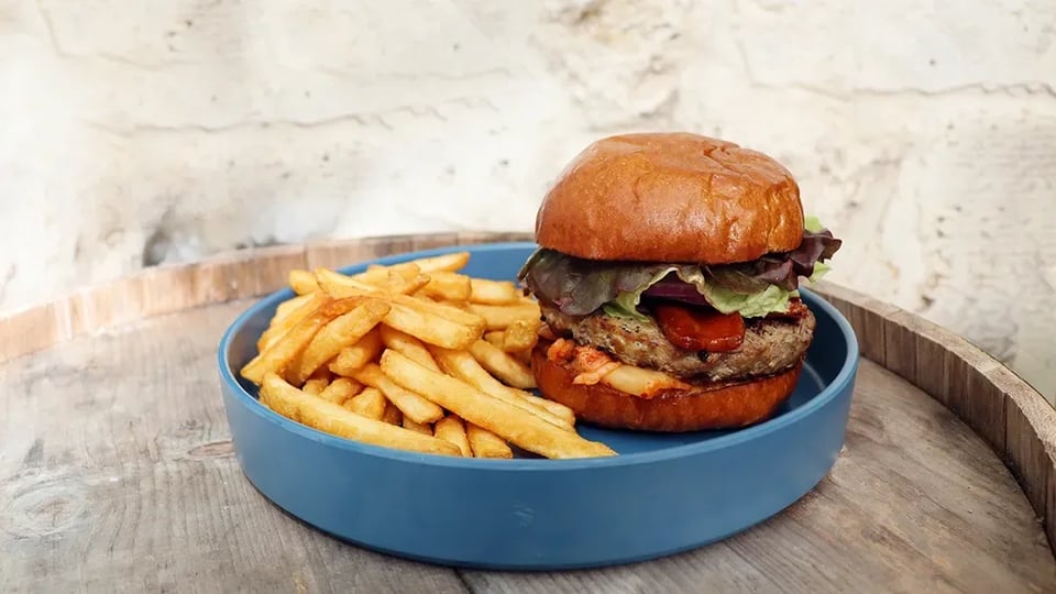 A burger with lettuce and fries on a blue plate set on a rustic wooden barrel table