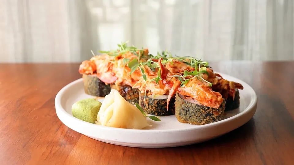 Sushi roll topped with spicy seafood and microgreens served with wasabi and pickled ginger on a white plate