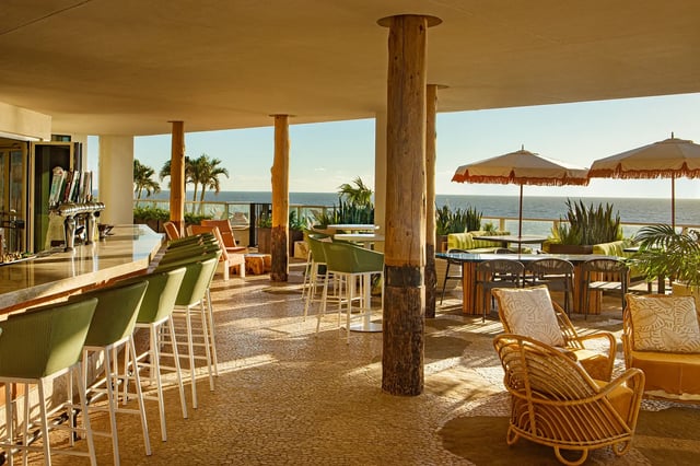 Open-air bar at Tesoro with green stools, rattan chairs and fringed umbrellas overlooking the Gulf at golden hour