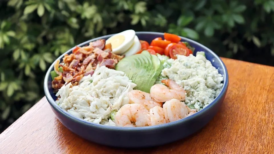 Cobb salad bowl with shrimp, crab, avocado, blue cheese, bacon, egg and tomatoes on a sunny outdoor table at Quinn's