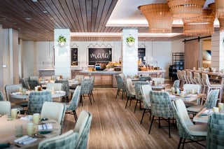 Bright dining room at Maia with woven pendant lights, blue-green woven chairs and a chalkboard sign above the buffet
