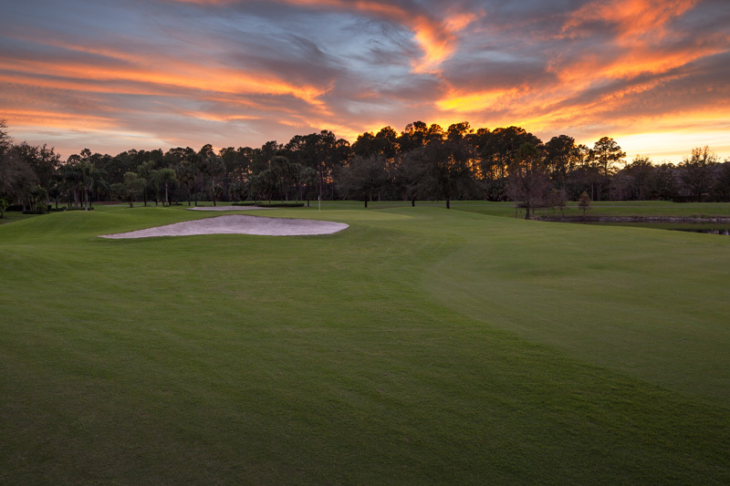 Sunset over the fairway and sand bunker at Arrowhead Golf Club, with pines silhouetted against orange clouds