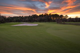 Sunset over the fairway and sand bunker at Arrowhead Golf Club, with pines silhouetted against orange clouds