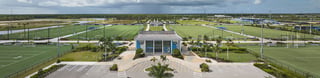 Aerial panorama of Paradise Coast Sports Complex showing green playing fields, palms and the covered stadium entrance