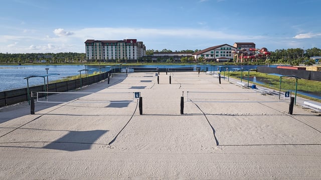 Rows of empty sand volleyball courts at Paradise Coast Sports Complex with a lake and hotels beyond