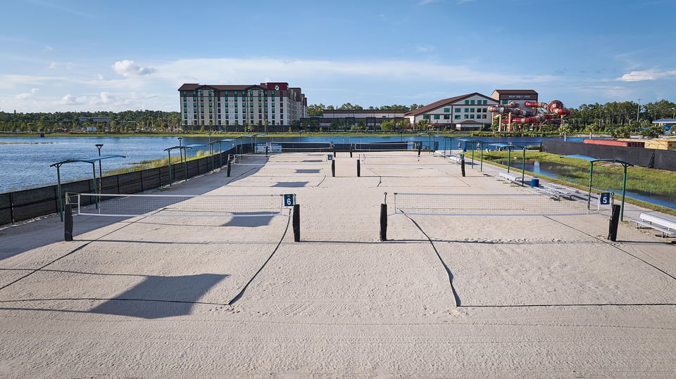 Rows of empty sand volleyball courts at Paradise Coast Sports Complex with a lake and hotels beyond