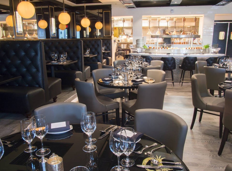 Upscale dining room at The Claw Bar with tufted black booths, gray armchairs, set tables and a lit open kitchen