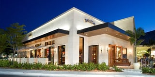 BrickTop's restaurant exterior lit up at dusk with white stone walls, patio umbrellas and palm trees