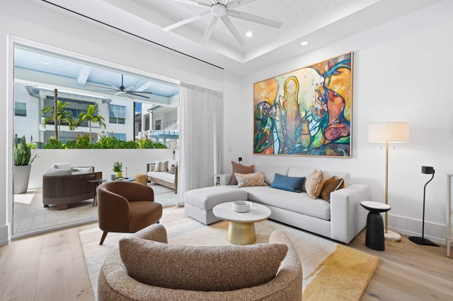 Bright modern living room with white sectional sofa, colorful abstract painting and sliding doors opening to a palm-shaded patio